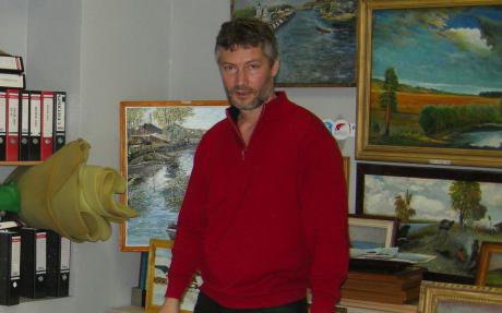 Roizman stands in his office in front of several paintings.