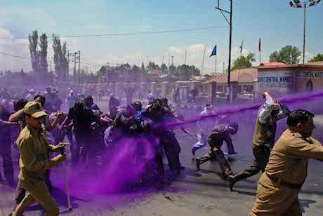 Indian police spray purple coloured water from water cannons at protesters. A jet of purple water directly hits some protesters