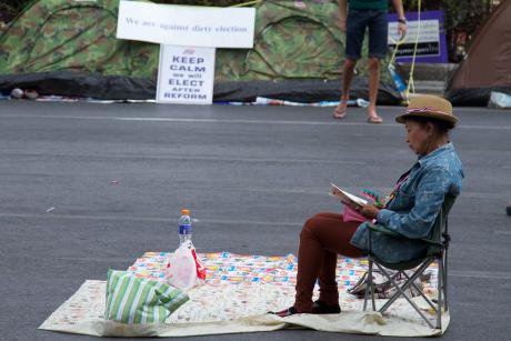 A Thai women sits peacefully in a chair in a street during a protest in Bangkok