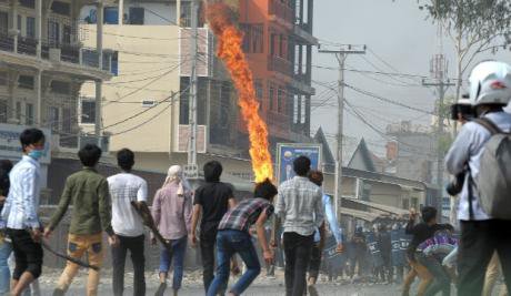 Ragged line of youths in a street facing off against line of soldiers. Fire in the air.