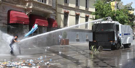 A man with a flag is directly hit by a stream of water from a police water cannon during Turky&#39;s Gezi Park protests