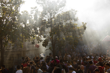 Light rays shine through trees onto Gezi Park crowds with objects caught in mid air
