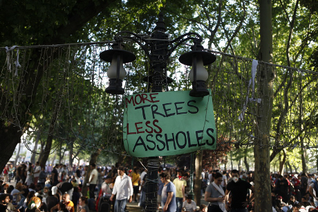 A mass of people fading in background with &#39;more trees less assholes&#39; banner at forefront.