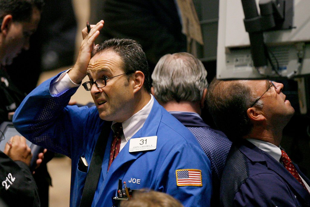 A trader on the New York Stock Exchange rubs his forehead and looks stressed