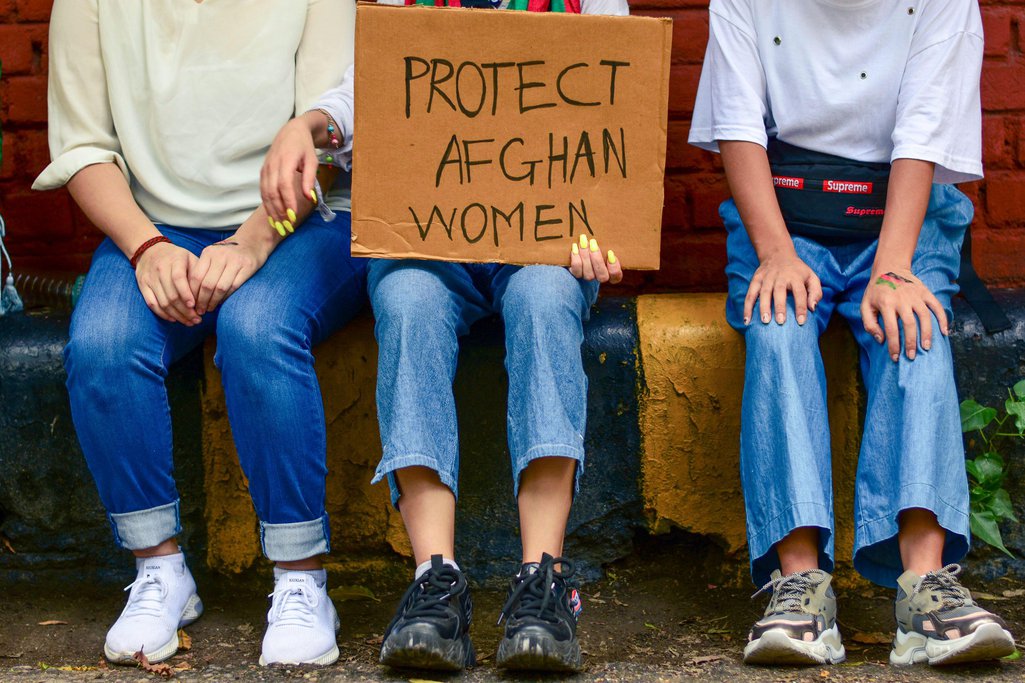 Três mulheres com o cartaz: Proteja mulheres afegãs