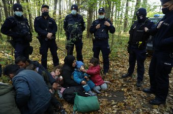 An Iraqi migrant woman with children sits on the ground as they are surrounded by border guards and police officers after they crossed the Belarusian-Polish border during the ongoing migrant crisis, in Hajnowka, Poland October 14, 2021