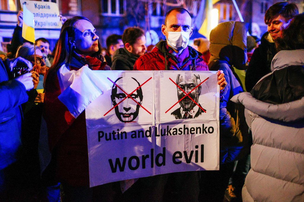 Protesters holding a placard with crossed-out portraits of Vladimir Putin and Belarusian dictator Alexander Lukashenka with slogans 