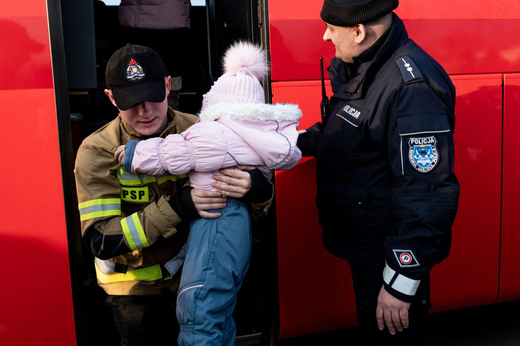 A Polish firefighter carries a young child off of a bus at the Tesco temporary refugee centre, 3 March 2022