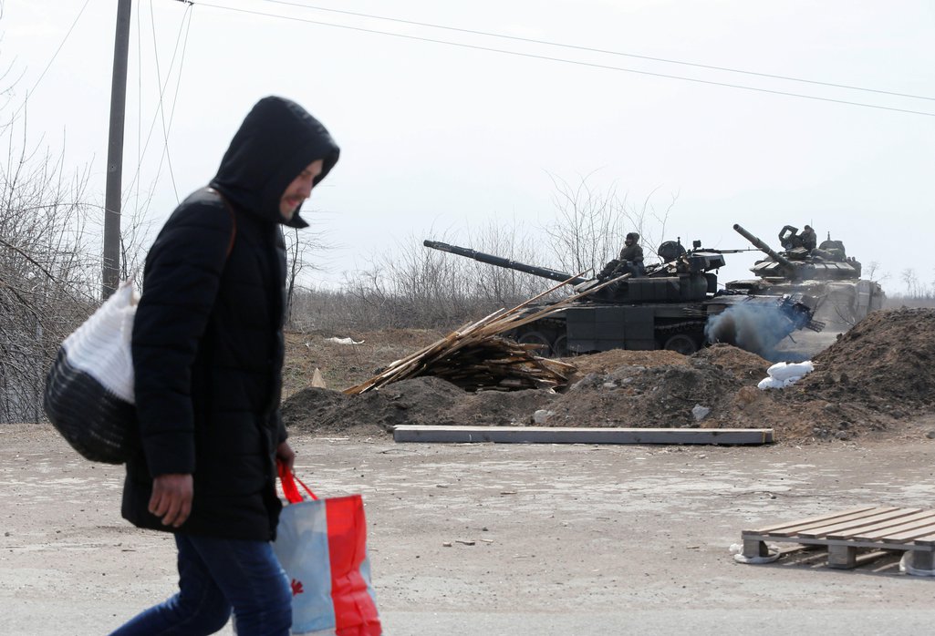 A man carries his belongings while walking along a road past tanks of pro-Russian troops during Ukraine-Russia conflict on the outskirts of the besieged southern port city of Mariupol, Ukraine, 20 March 2022
