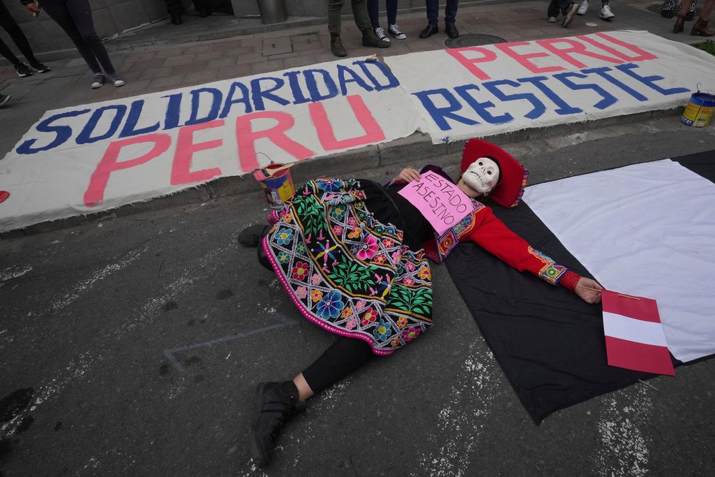 A woman with a mask lays down on the ground with a sign that reads in Spanish holds 