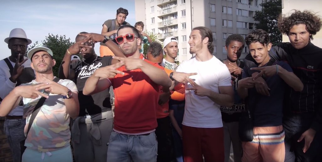 Ademo (orange T-shirt) and N.O.S (white T-shirt) and their entourage forming with their hands a “Z” signifying “le zoo”, to describe their hood, Les Tarterêts, in the 2015 debut single Le monde ou rien (The world or nothing) viewed over 100 million times