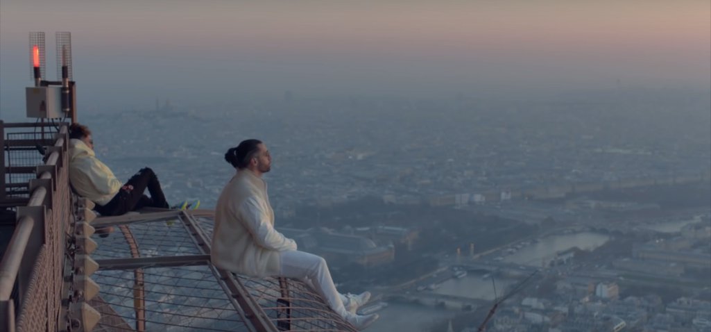 Ademo (white jeans) and N.O.S (black jeans) sitting on the top of the Eiffel Tower at dawn.
