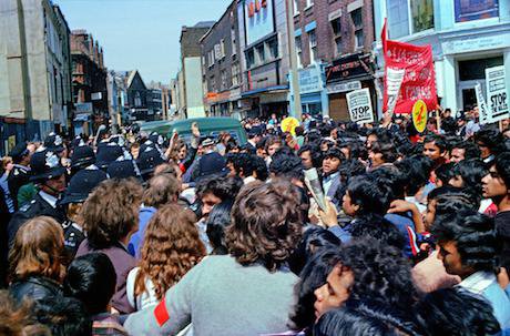 lead Crowd of young Bengali men fill East London street. Police officers in background.