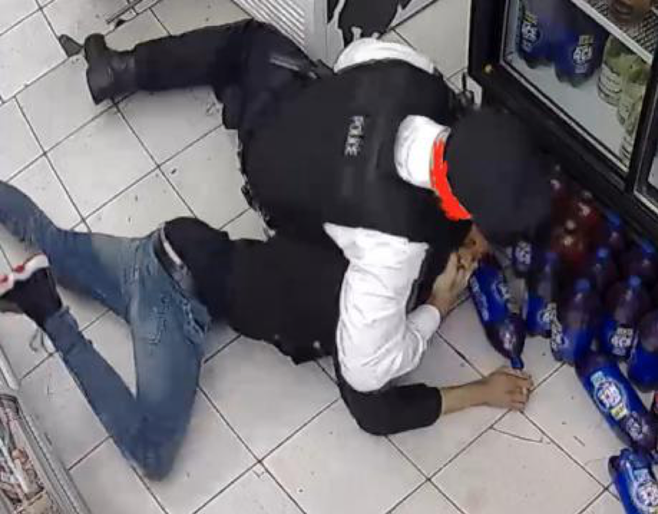 Policeman holds young man on ground of convenience shop