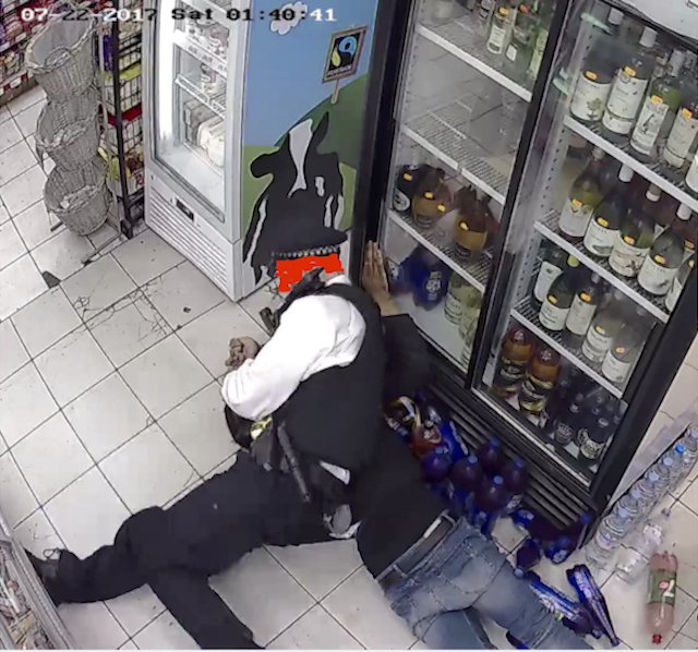 Police officer holding young man in headlock on the floor of a small shop.