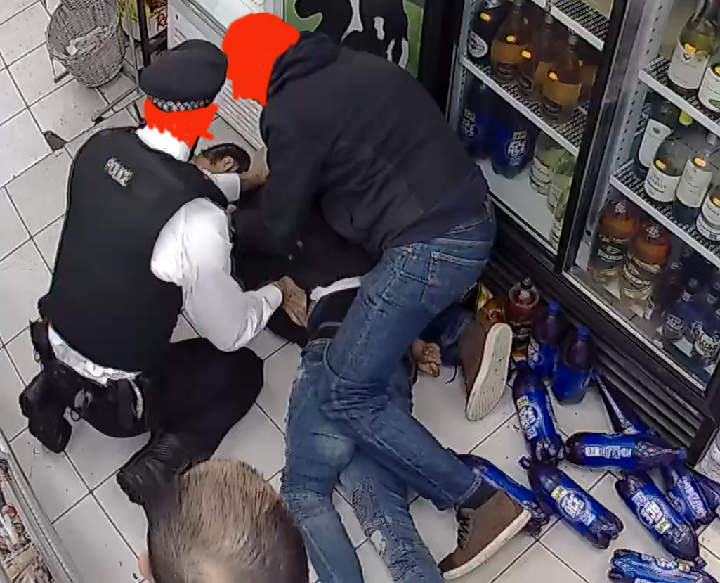 Two men kneel on a young man lying on a shop floor.