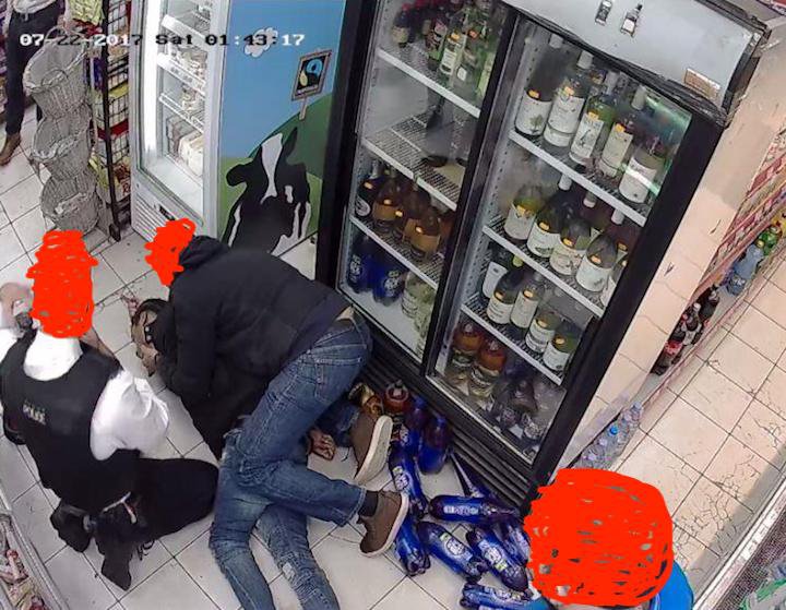 Rashan lying on the shop floor, held down by man in hoody and police kneels by his side.