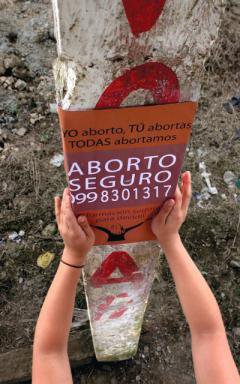 Hands post a flyer on a post. Flyer says &#39;Aborto Seguro&#39;