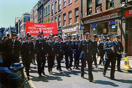 Police officers line up in front of protestors on Brick Lane