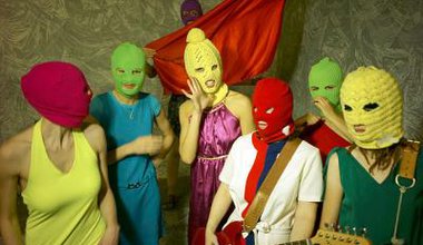 The 6 members of Pussy Riot pose with a guitar and colourful knitted masks on their heads.