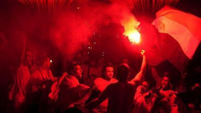 Black and red photo of men lit by a flare. Flag and flare held up.