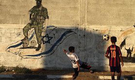 Palestinian boys play football in front of anti-Israel graffiti, Gaza City, 2011. Demotix/Majdi Fathi. All rights reserved.