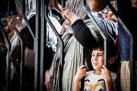 A boy from Iraq stands with his family at the gate of the registration centre in Kos. Stephen Ryan:Flickr. Some rights reserved.jpg