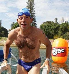 Hairy-chested man in swim cap and speedos exits a lake