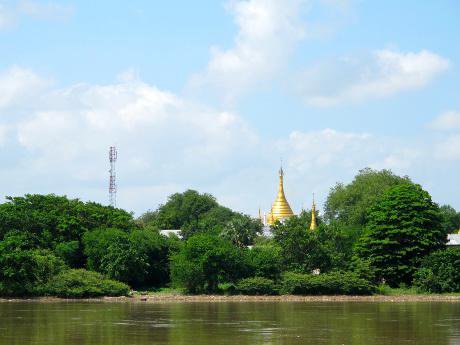 A mobile phone antenna and golden temple behind green trees alongside a river