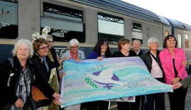 Women hold a WILPF banner in front of a train