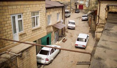 View of modern Derbent. Several cars are parked haphazardly on a cracked street. 