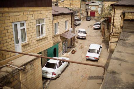 View of modern Derbent. Several cars are parked haphazardly on a cracked street. 