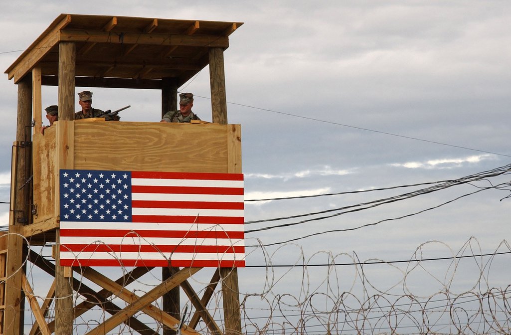 An American flag is draped over the side of a watchtower manned by armed guards