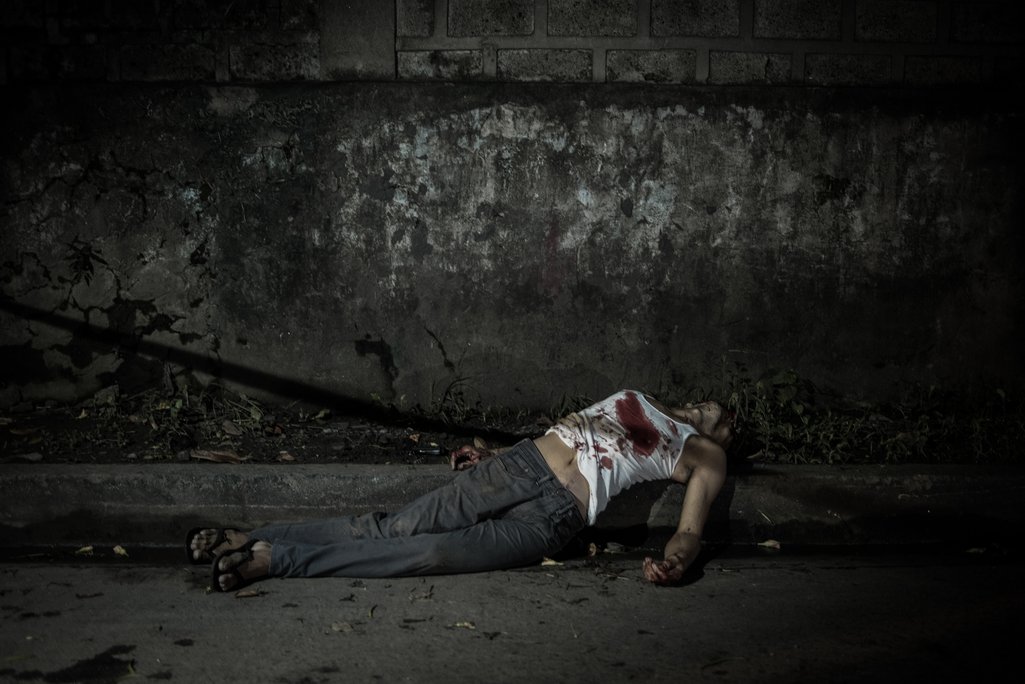 A bloodied lifeless body lies on a street.