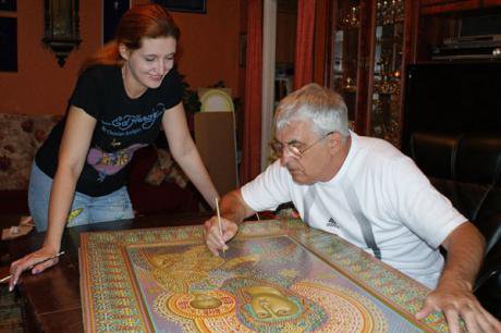A an paints a religious icon as a young woman looks on admiringly.