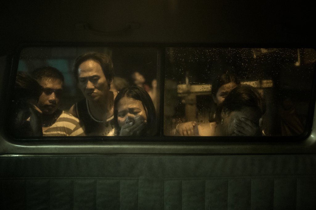 Dimly lit people looking through a window, one of them a woman crying.