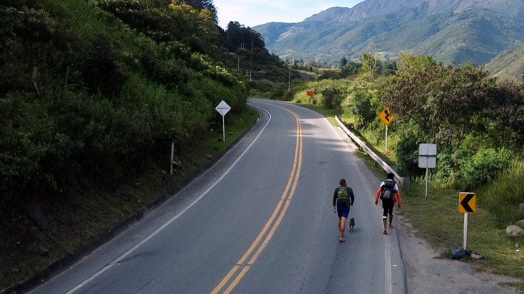 Christhoper, Kember e Troya caminham à beira de uma estrada colombiana
