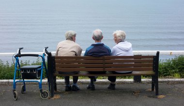 Two elderly men and an elderly woman sitting on bench overlooking sea. Saltburn by the Sea, North Yorkshire, England, UK