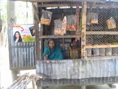 A women sitting in a corrugated iron shack surrounded by produce and items for sale