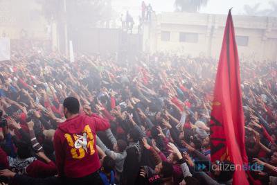 Crowd of men in mist with a large flag. All hands raised in a salute.
