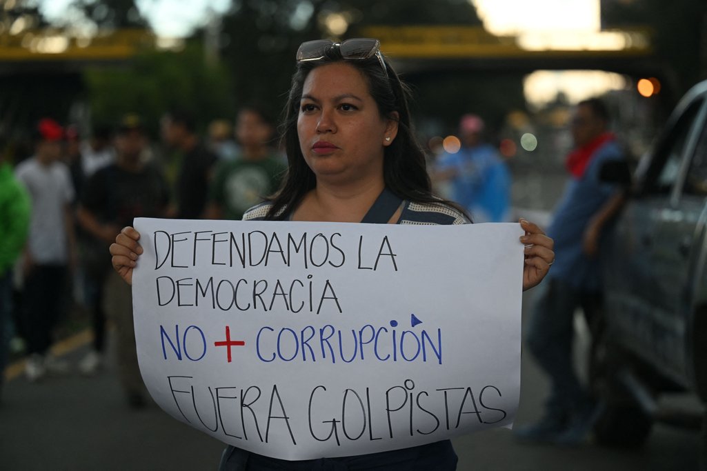 Una mujer sostiene un cartel que dice: Defendamos la democracia. No más corrupción. Fuera golpistas