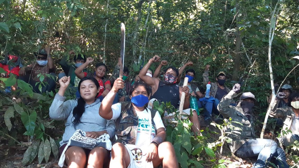 Indígenas Guajajara posam para foto na TI Arariboia. Durante a pandemia de Covid-19, quase todos usam máscaras nos deslocamentos pela selva. Um deles, ao fundo, com máscara azul, exibe para a câmera um frasco de álcool em gel
