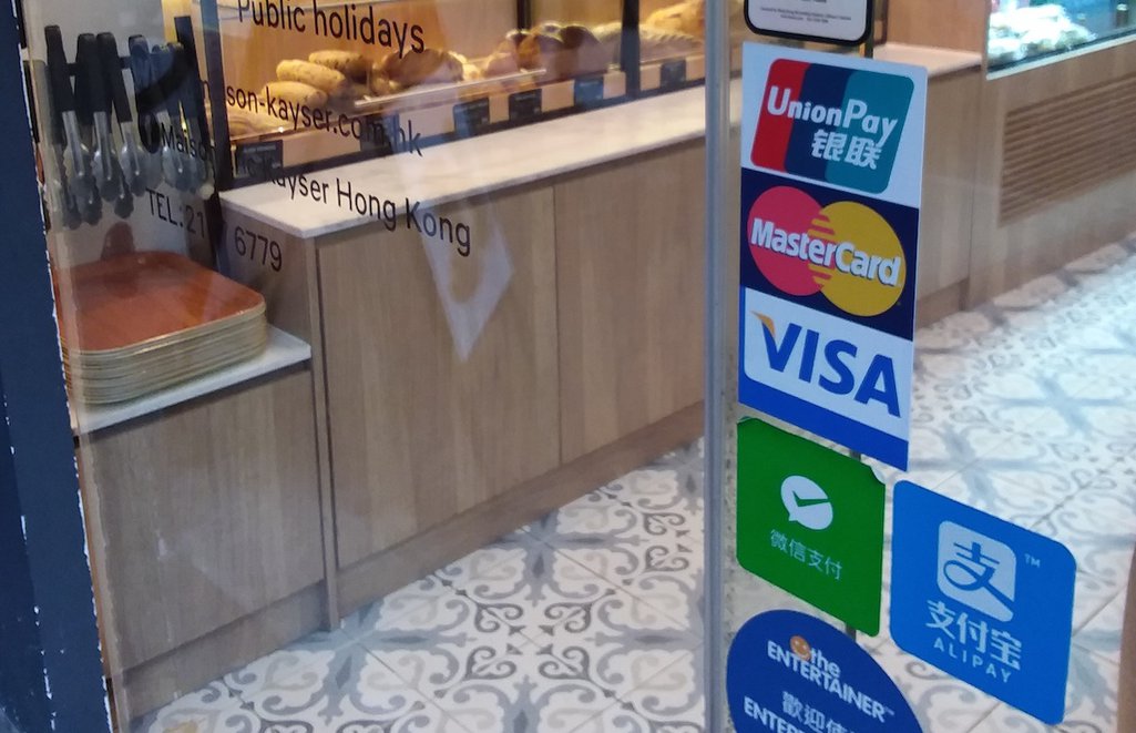 WeChat and AliPay stickers next to Visa and Mastercard on a bakery window illustrate the changing payments landscape.