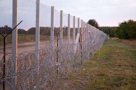 A long, tall wire fence with barbed wire running through a field.