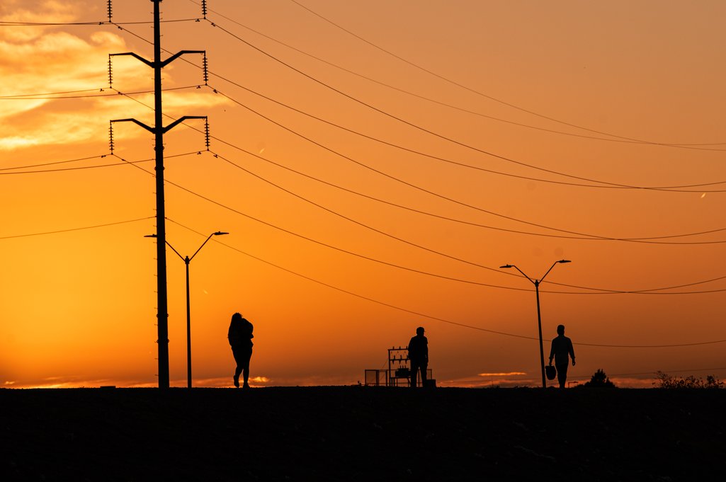Plano general a contra luz de tres migrantes caminando cerca de la valla fronteriza en Ciudad Juarez, México