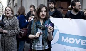 Women holds up a credit card and scissors, surrounded by campaigners