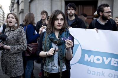 Women holds up a credit card and scissors, surrounded by campaigners