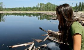 Woman holds an oil-covered branch in front of an oil spill