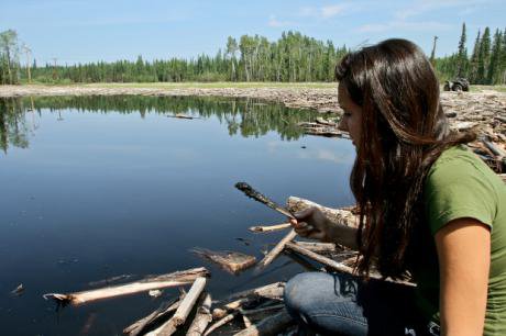 Woman holds an oil-covered branch in front of an oil spill