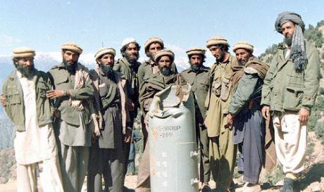A group of armed mujahideen pose for the camera in front of a Soviet bomb case.